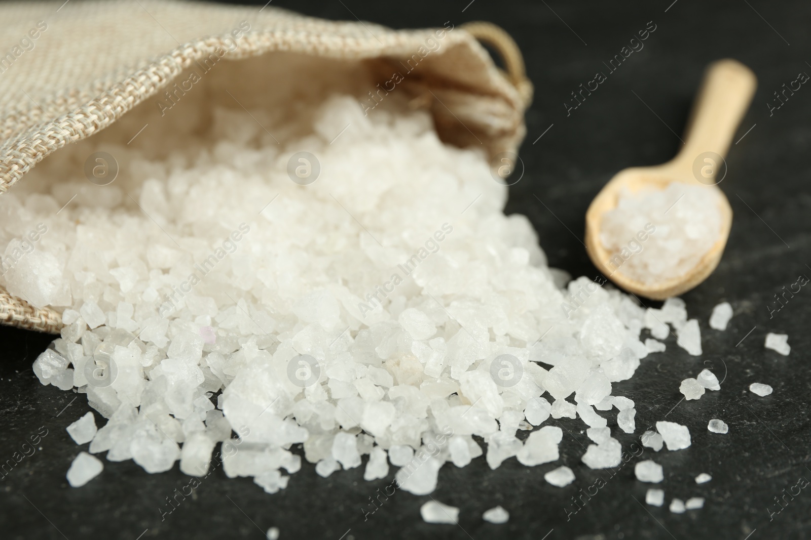 Photo of Sea salt, bag and spoon on dark gray textured table, closeup