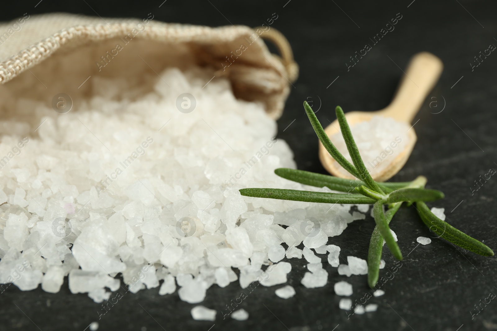 Photo of Sea salt and rosemary on dark gray textured table, closeup