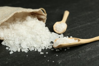 Sea salt, bag and spoons on dark gray textured table, closeup