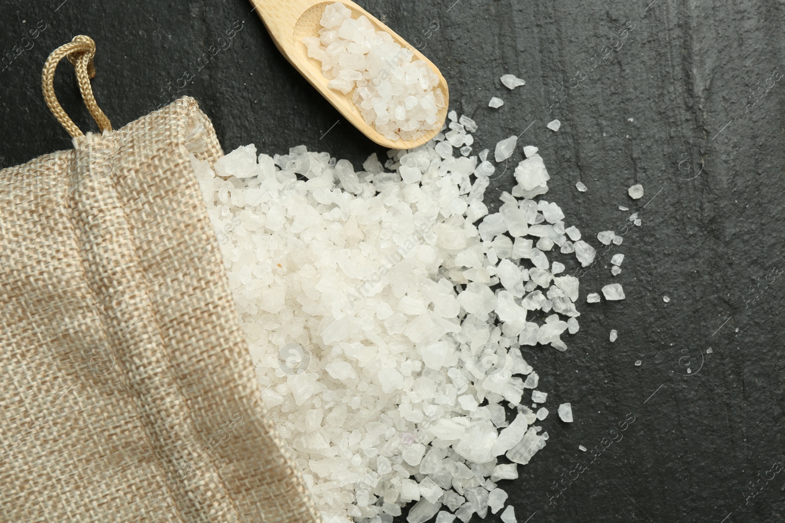 Photo of Sea salt, bag and spoon on dark gray textured table, flat lay