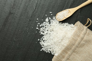 Photo of Sea salt, bag and spoon on dark gray textured table, flat lay. Space for text