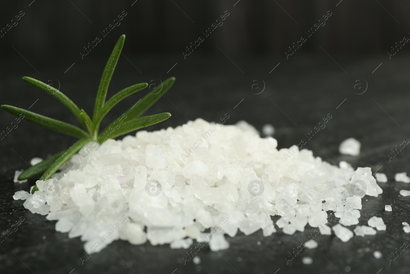 Photo of Sea salt and rosemary on dark gray textured table, closeup