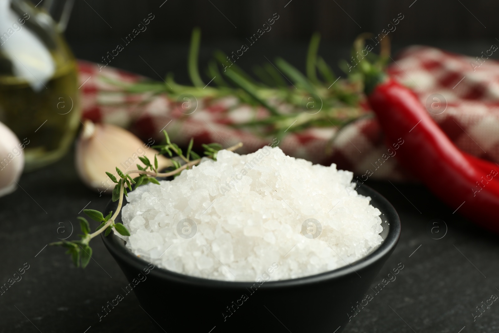 Photo of Sea salt and thyme in bowl on dark gray table, closeup