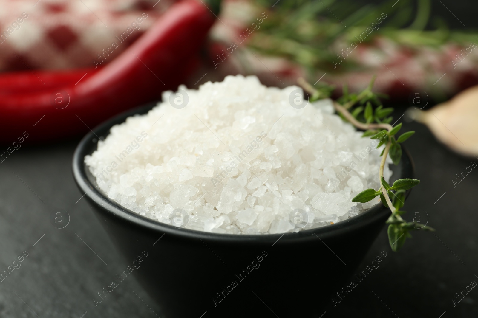 Photo of Sea salt and thyme in bowl on dark gray table, closeup