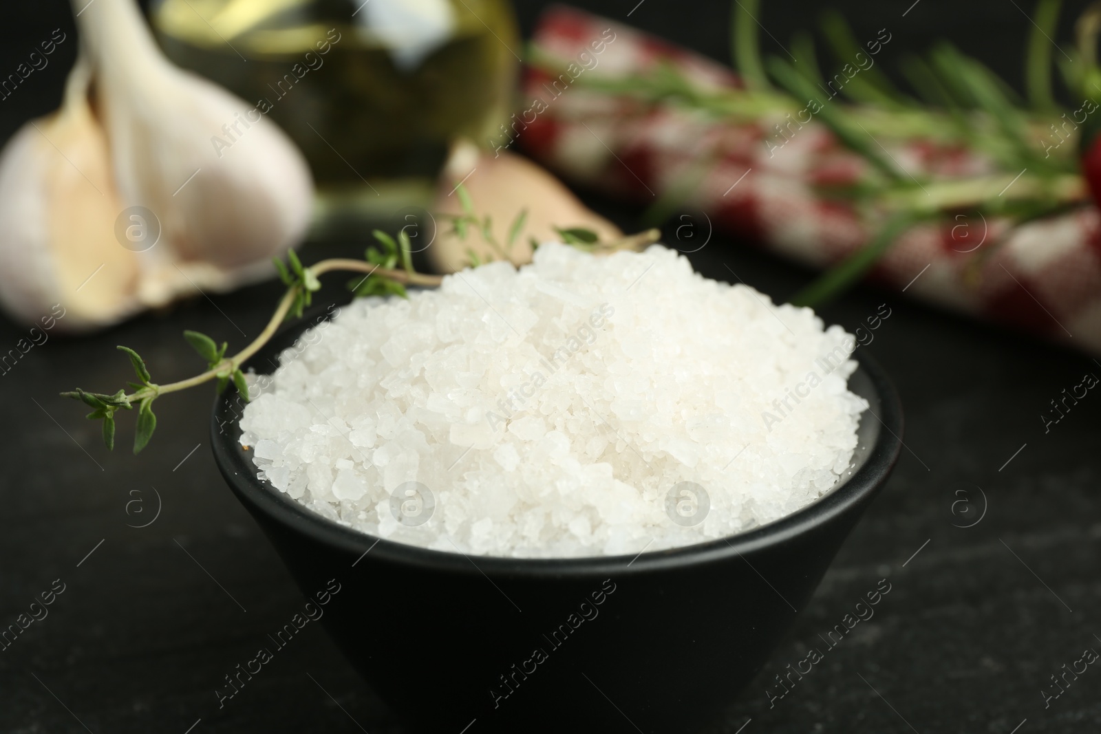 Photo of Sea salt and thyme in bowl on dark gray table, closeup