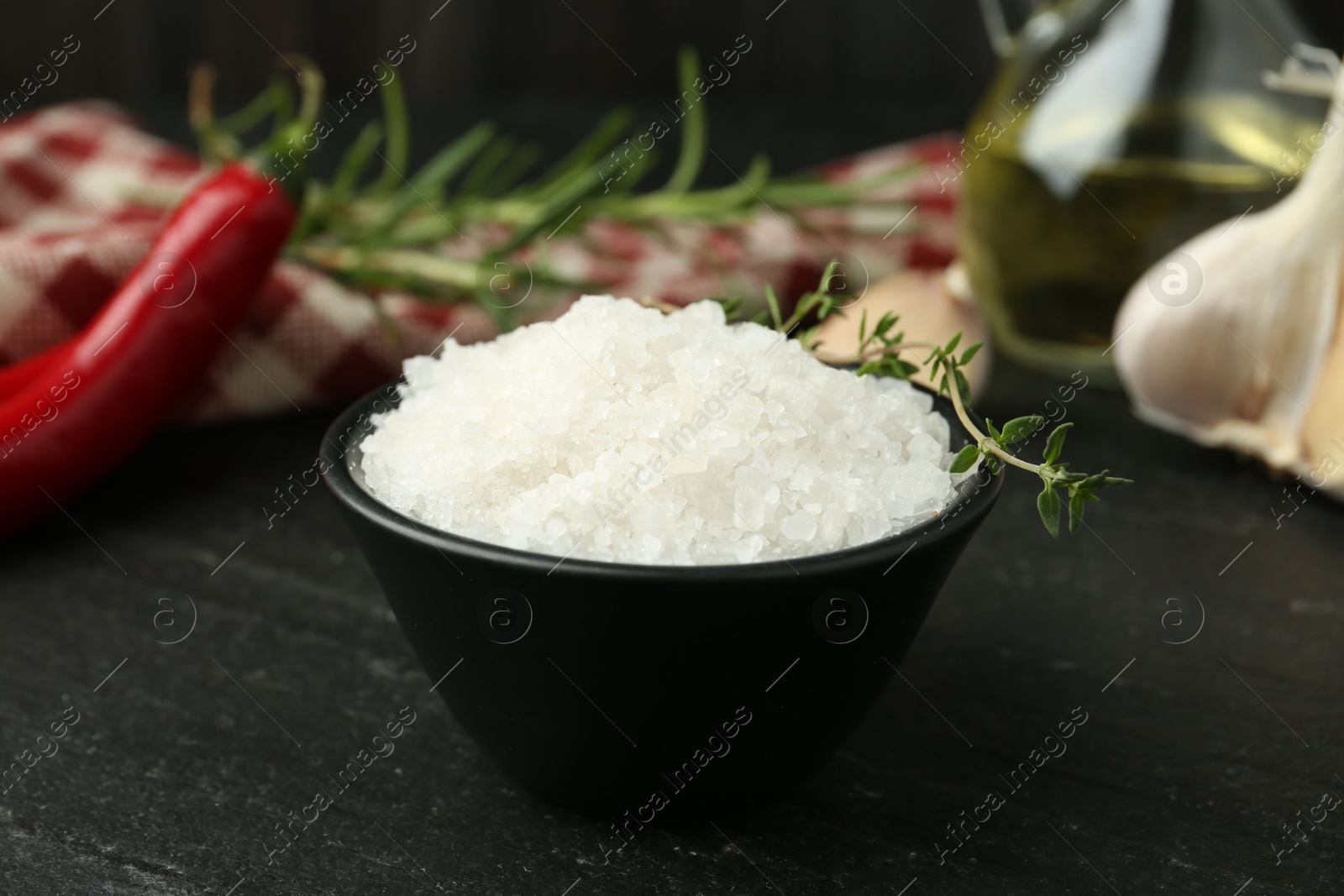 Photo of Sea salt and thyme in bowl on dark gray textured table, closeup