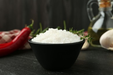 Photo of Sea salt and thyme in bowl on dark gray textured table, closeup