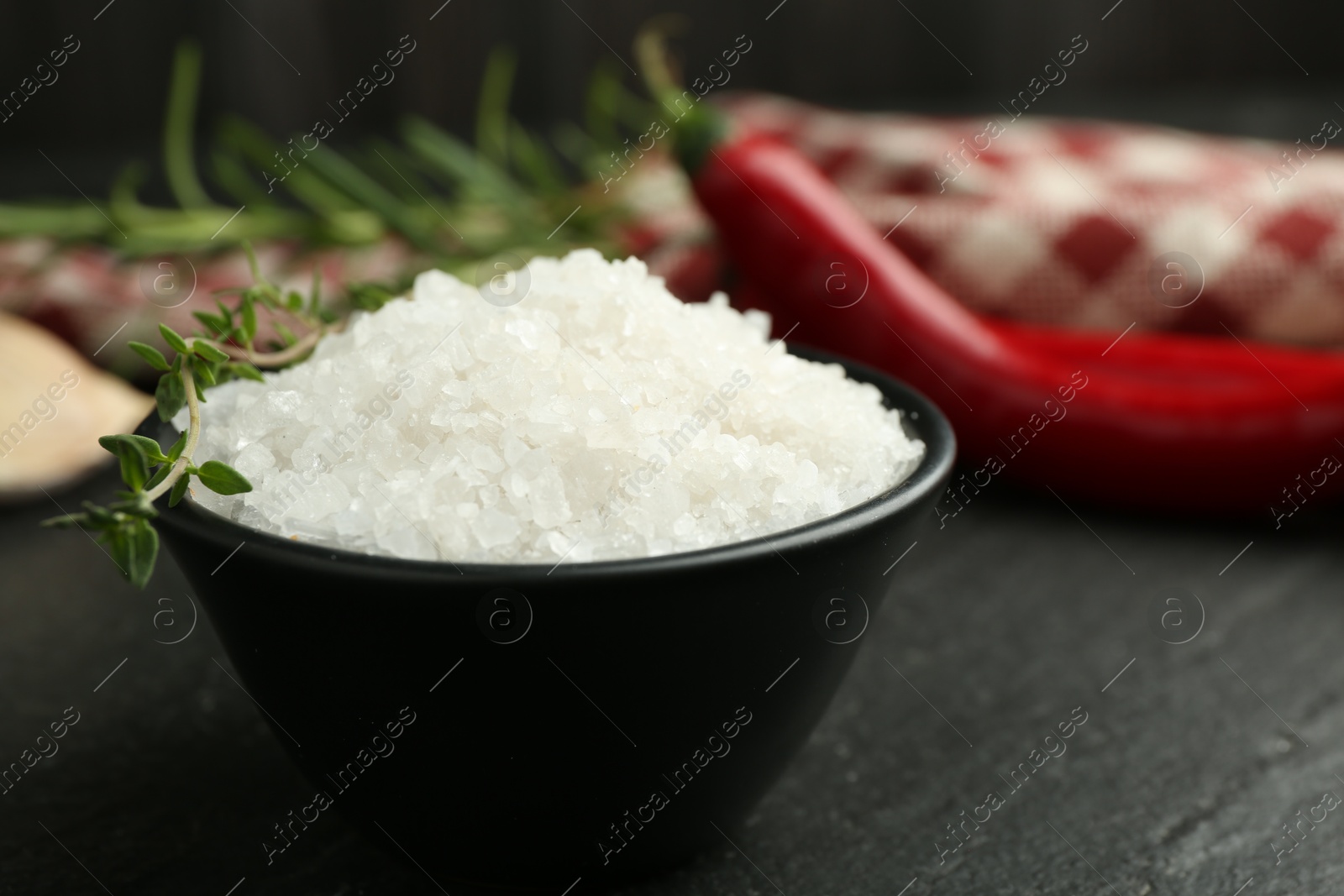 Photo of Sea salt and thyme in bowl on dark gray table, closeup