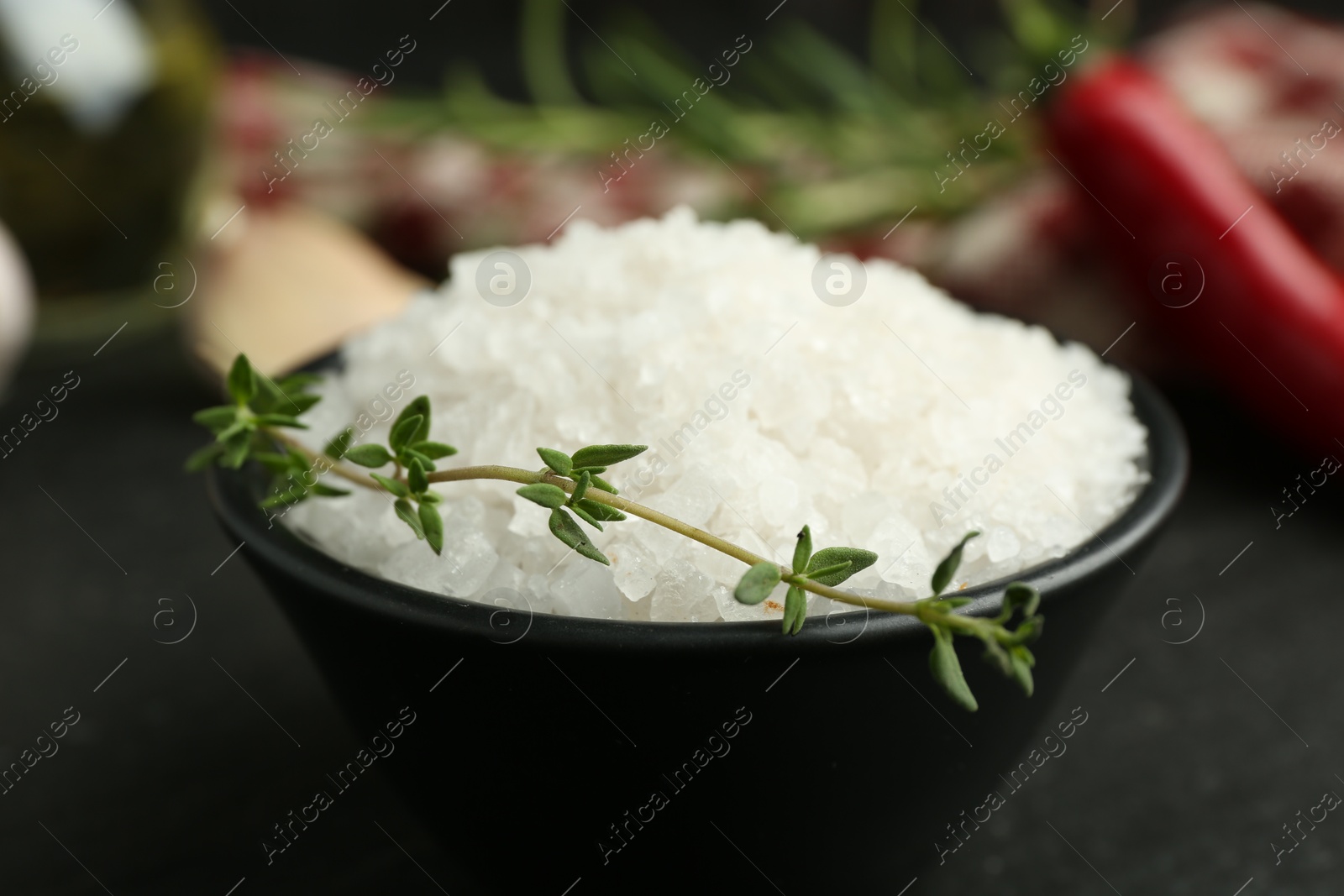 Photo of Sea salt and thyme in bowl on dark gray table, closeup