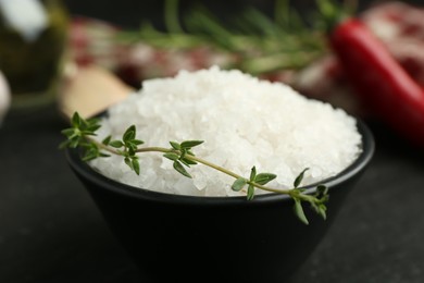 Photo of Sea salt and thyme in bowl on dark gray table, closeup