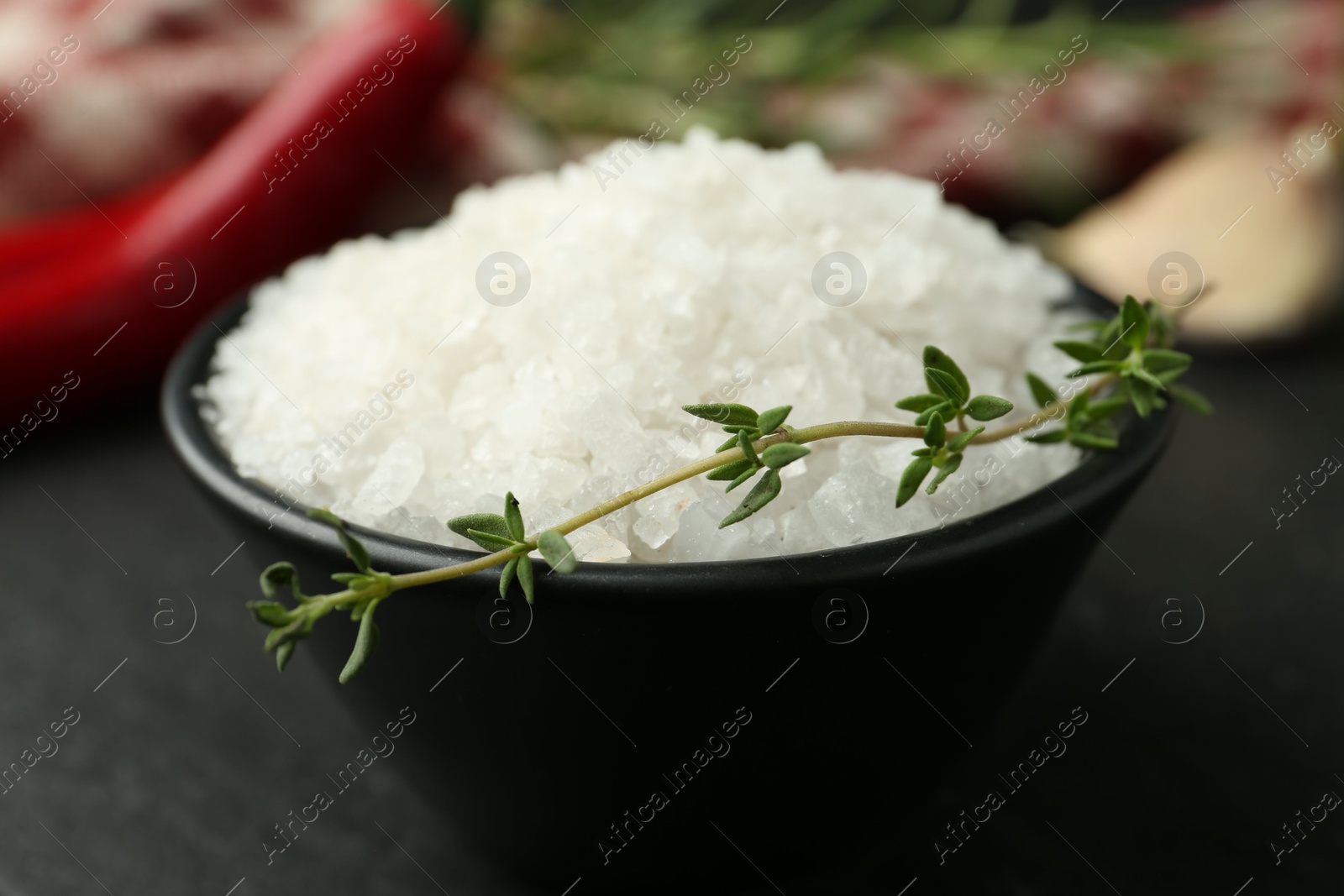 Photo of Sea salt and thyme in bowl on dark gray table, closeup