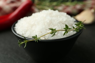 Photo of Sea salt and thyme in bowl on dark gray table, closeup