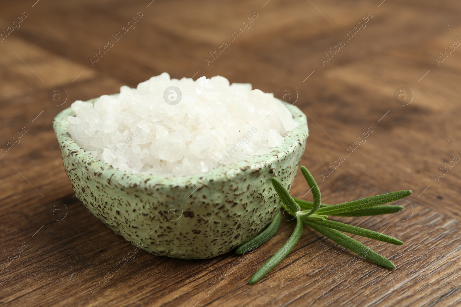 Photo of Sea salt and rosemary in bowl on wooden table, closeup