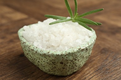 Photo of Sea salt and rosemary in bowl on wooden table, closeup