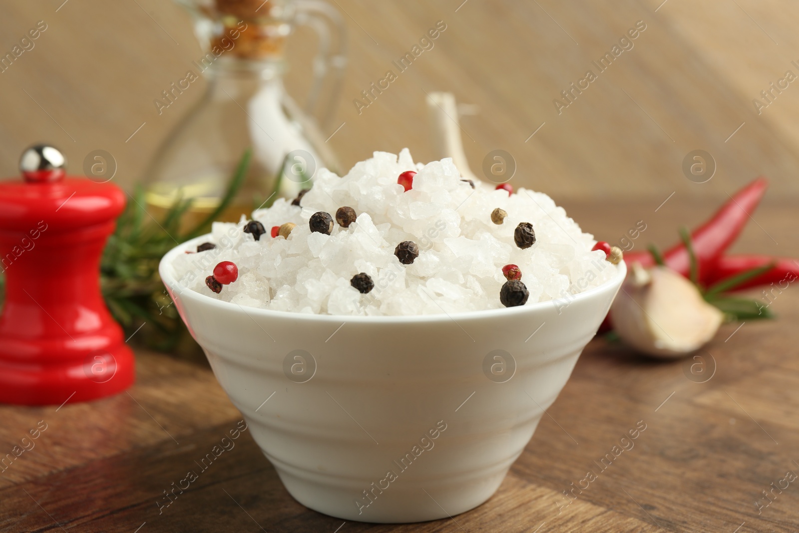 Photo of Sea salt and spices in bowl on wooden table, closeup