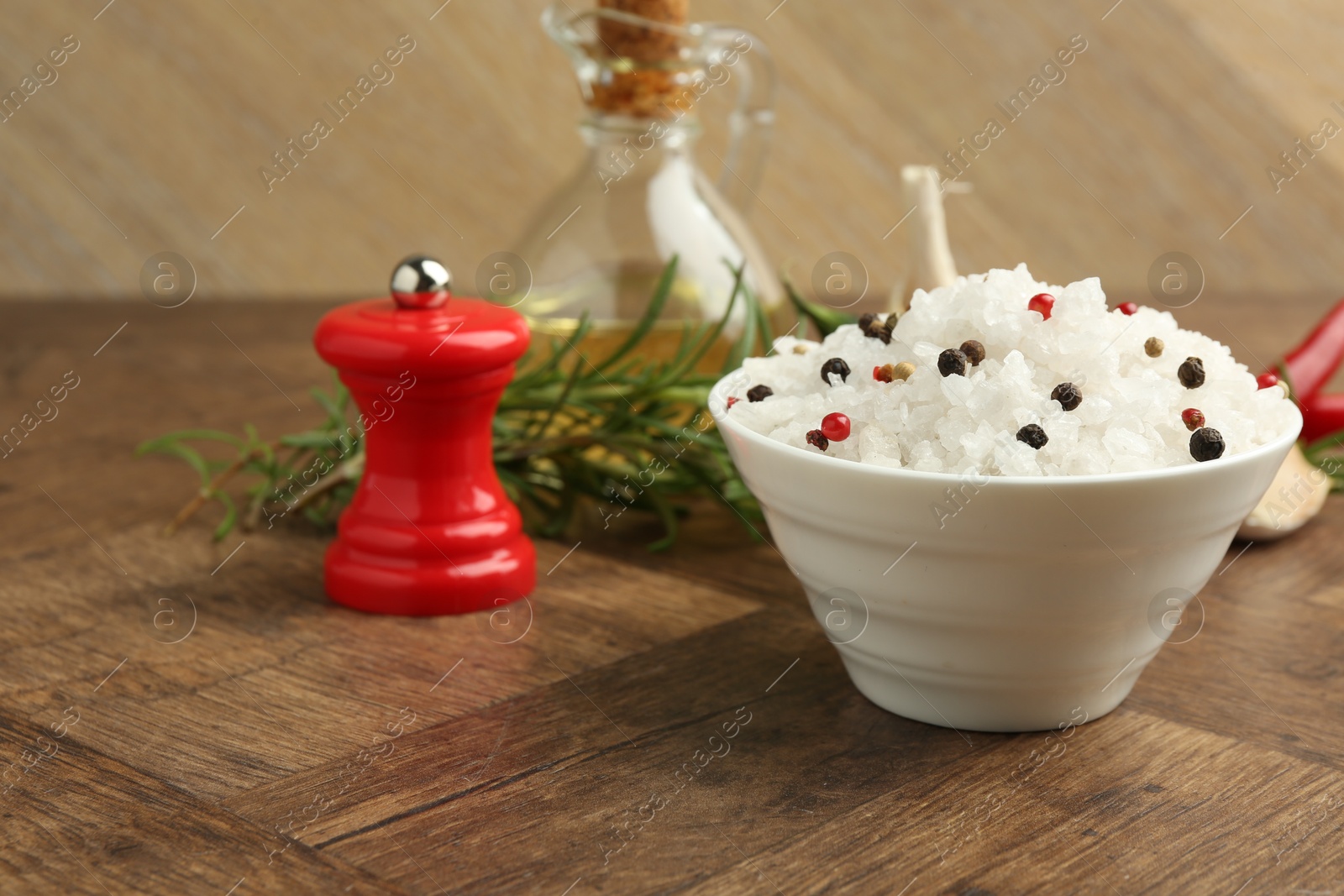 Photo of Sea salt in bowl and spices on wooden table, closeup