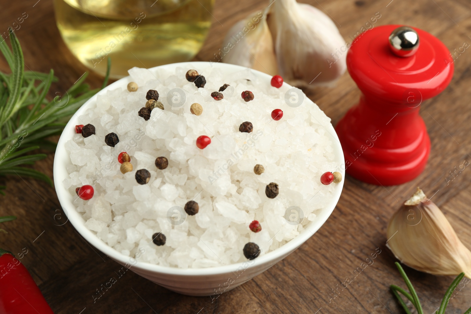 Photo of Sea salt in bowl and spices on wooden table, closeup