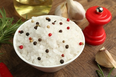 Sea salt in bowl and spices on wooden table, closeup