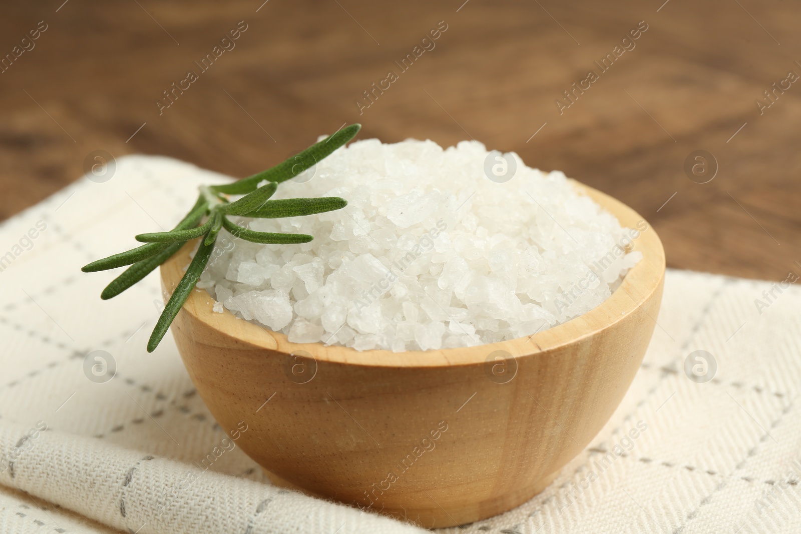 Photo of Sea salt and rosemary in bowl on brown table, closeup