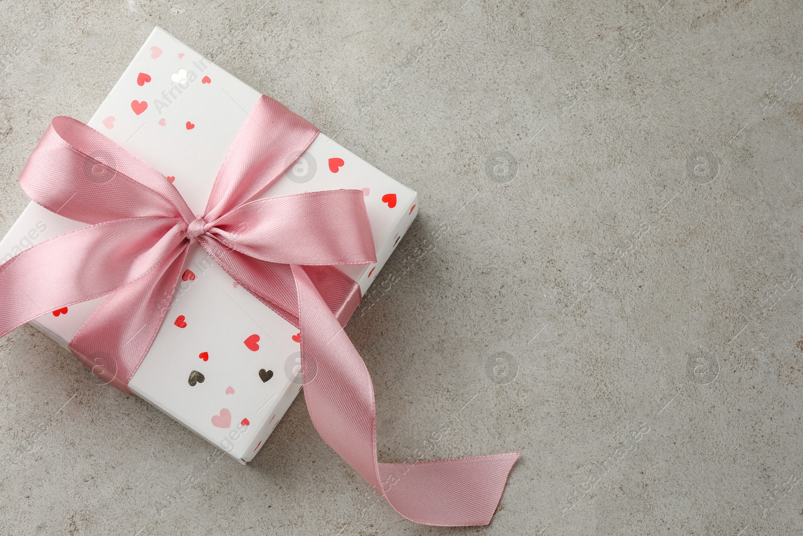 Photo of Beautiful gift box with pink ribbon on light grey table, top view. Space for text