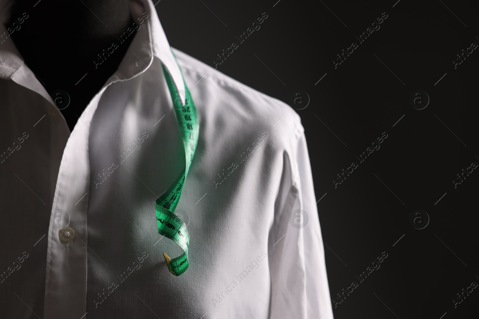 Photo of Male mannequin with white shirt and measuring tape on black background, closeup. Space for text