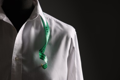 Photo of Male mannequin with white shirt and measuring tape on black background, closeup. Space for text