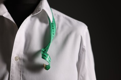 Male mannequin with white shirt and measuring tape on black background, closeup