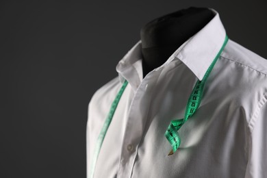 Male mannequin with white shirt and measuring tape on grey background, closeup. Space for text