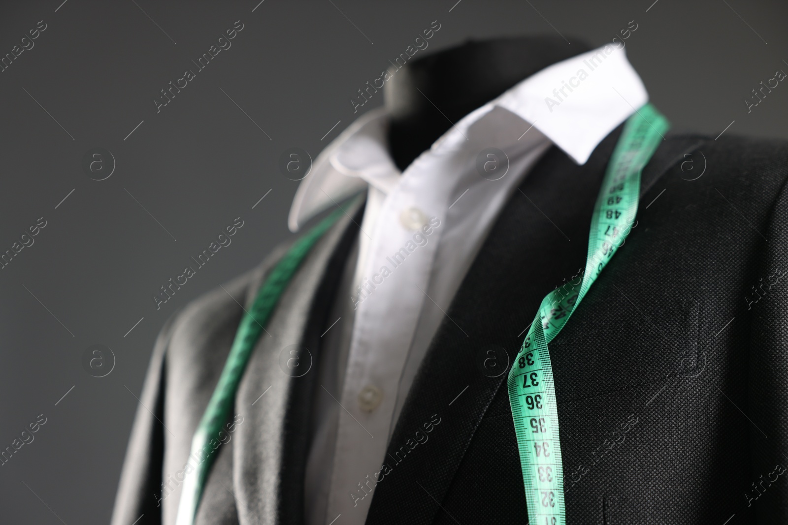 Photo of Male mannequin with jacket, white shirt and measuring tape on grey background, closeup