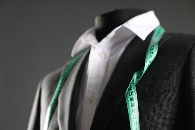 Male mannequin with jacket, white shirt and measuring tape on grey background, closeup