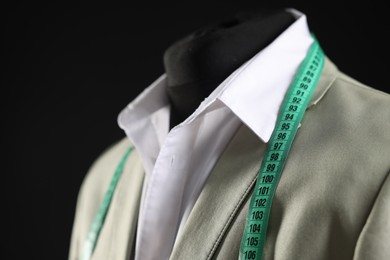 Male mannequin with jacket, shirt and measuring tape on black background, closeup