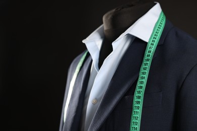 Photo of Male mannequin with jacket, shirt and measuring tape on black background, closeup. Space for text