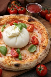 Delicious pizza with burrata cheese, basil, sauce and tomatoes on table, closeup