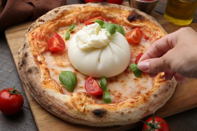 Woman adding basil to burrata pizza at wooden table, closeup