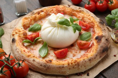 Delicious pizza with burrata cheese, basil and tomatoes on table, closeup