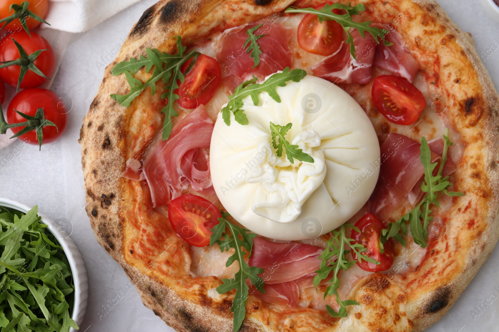 Photo of Delicious pizza with burrata cheese, arugula, tomatoes and ham on table, top view