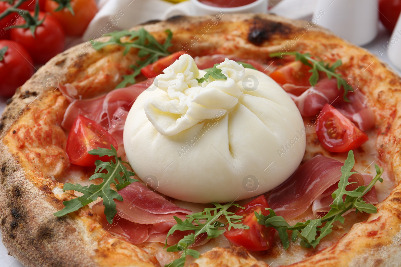 Photo of Delicious pizza with burrata cheese, arugula, tomatoes and ham on table, closeup