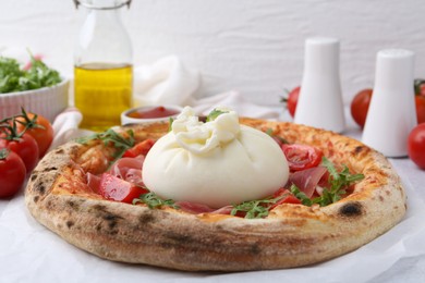 Photo of Delicious pizza with burrata cheese, arugula, tomatoes and ham on table, closeup