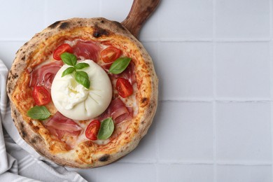 Delicious pizza with burrata cheese, basil, tomato and ham on white tiled table, top view. Space for text