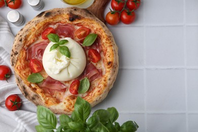 Photo of Delicious pizza with burrata cheese, basil, tomatoes and ham on white tiled table, top view. Space for text