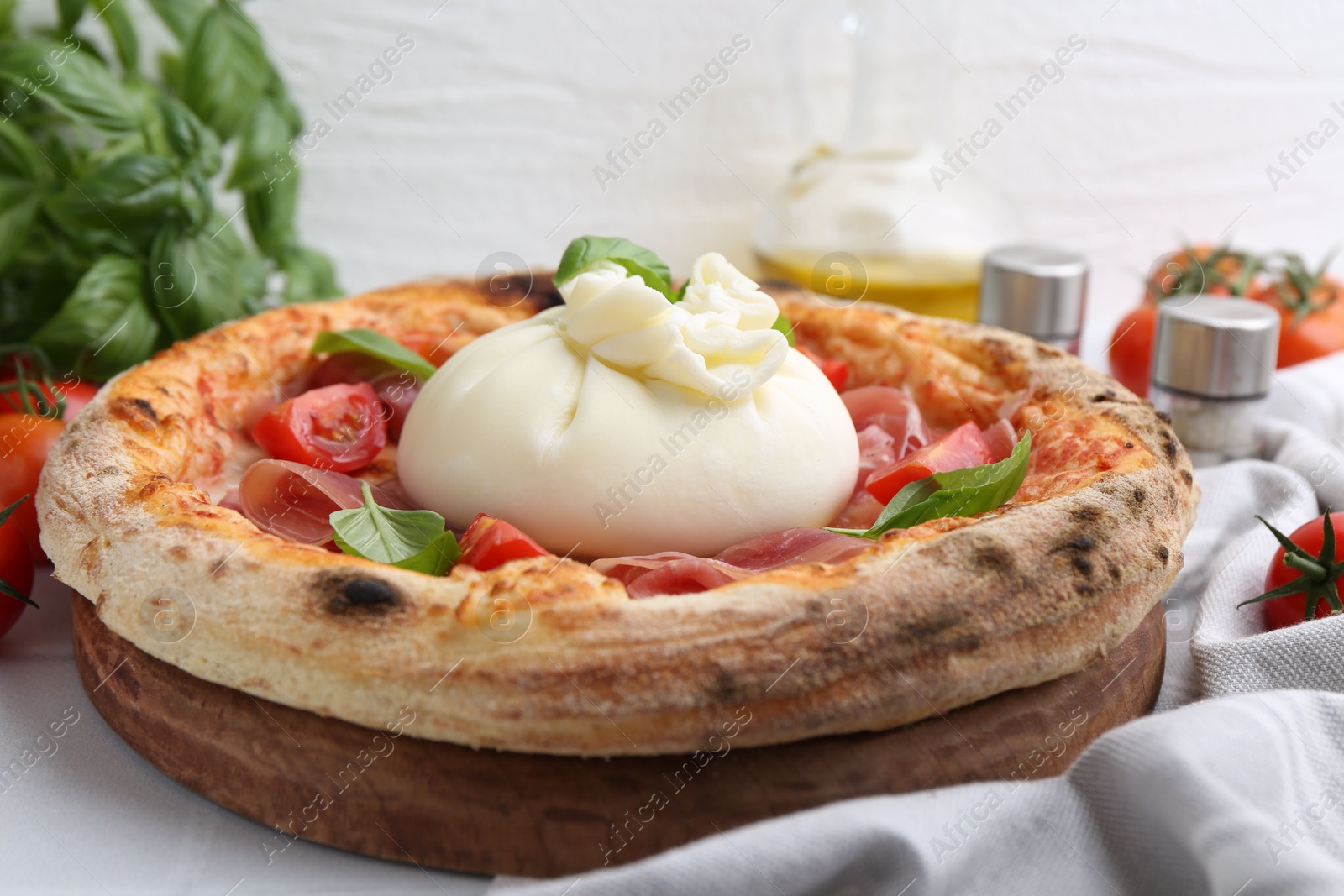 Photo of Delicious pizza with burrata cheese, basil, tomatoes and ham on table, closeup