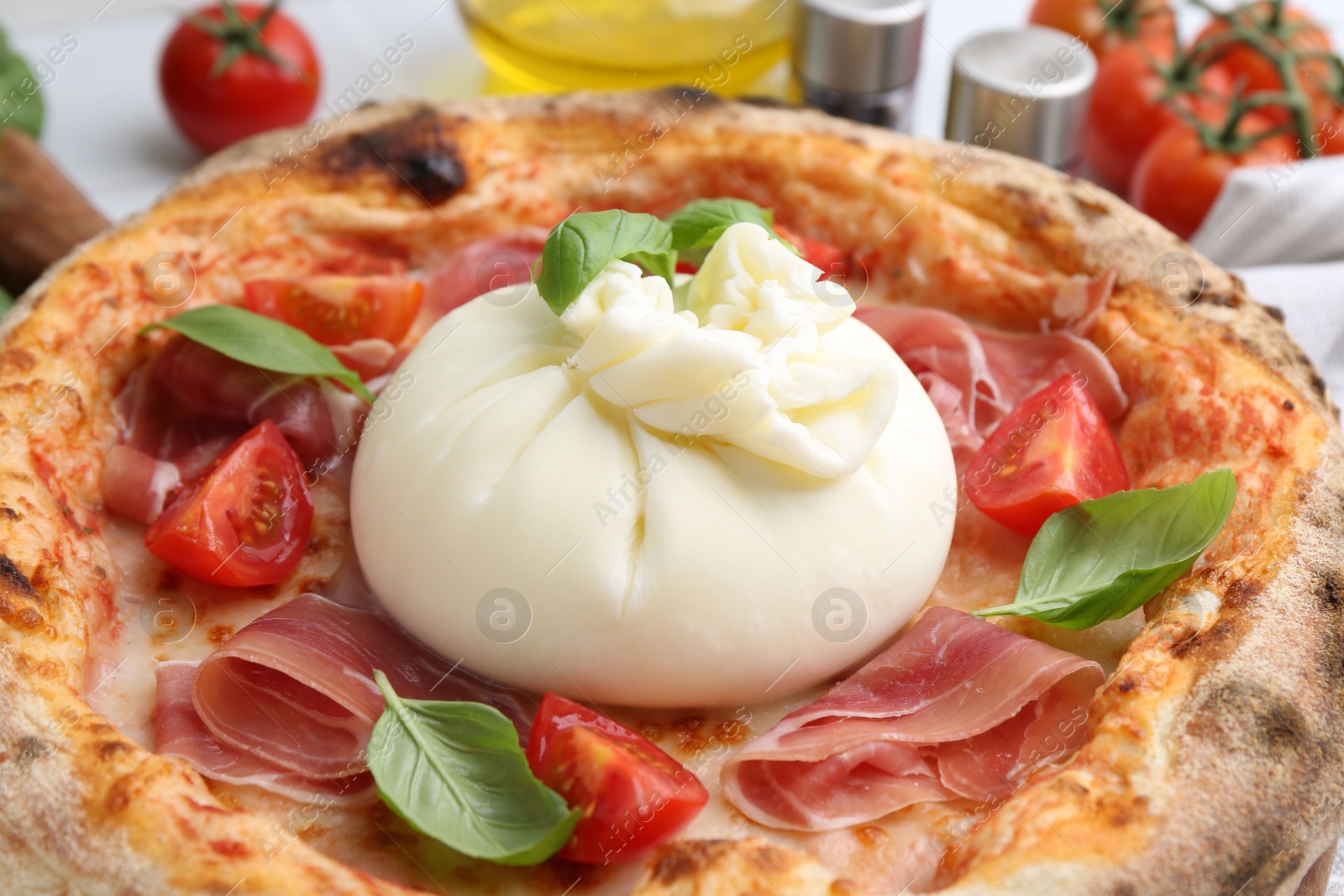 Photo of Delicious pizza with burrata cheese, basil, tomatoes and ham on table, closeup