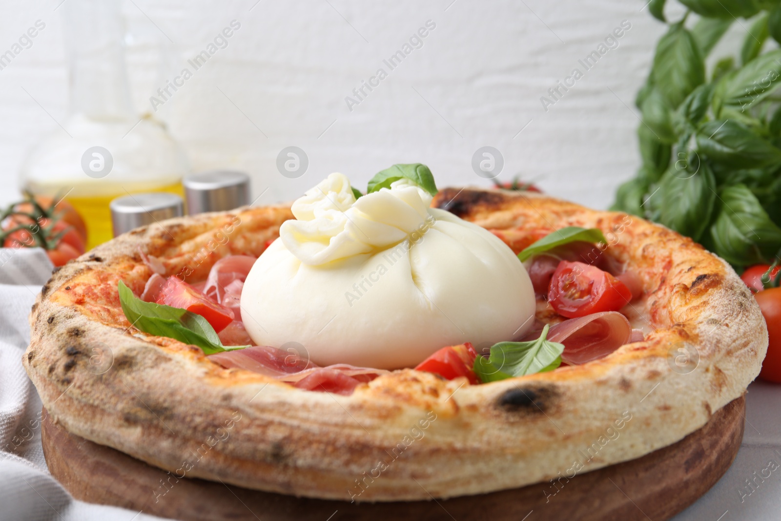 Photo of Delicious pizza with burrata cheese, basil, tomatoes and ham on table, closeup