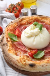 Delicious pizza with burrata cheese, basil, tomatoes and ham on table, closeup