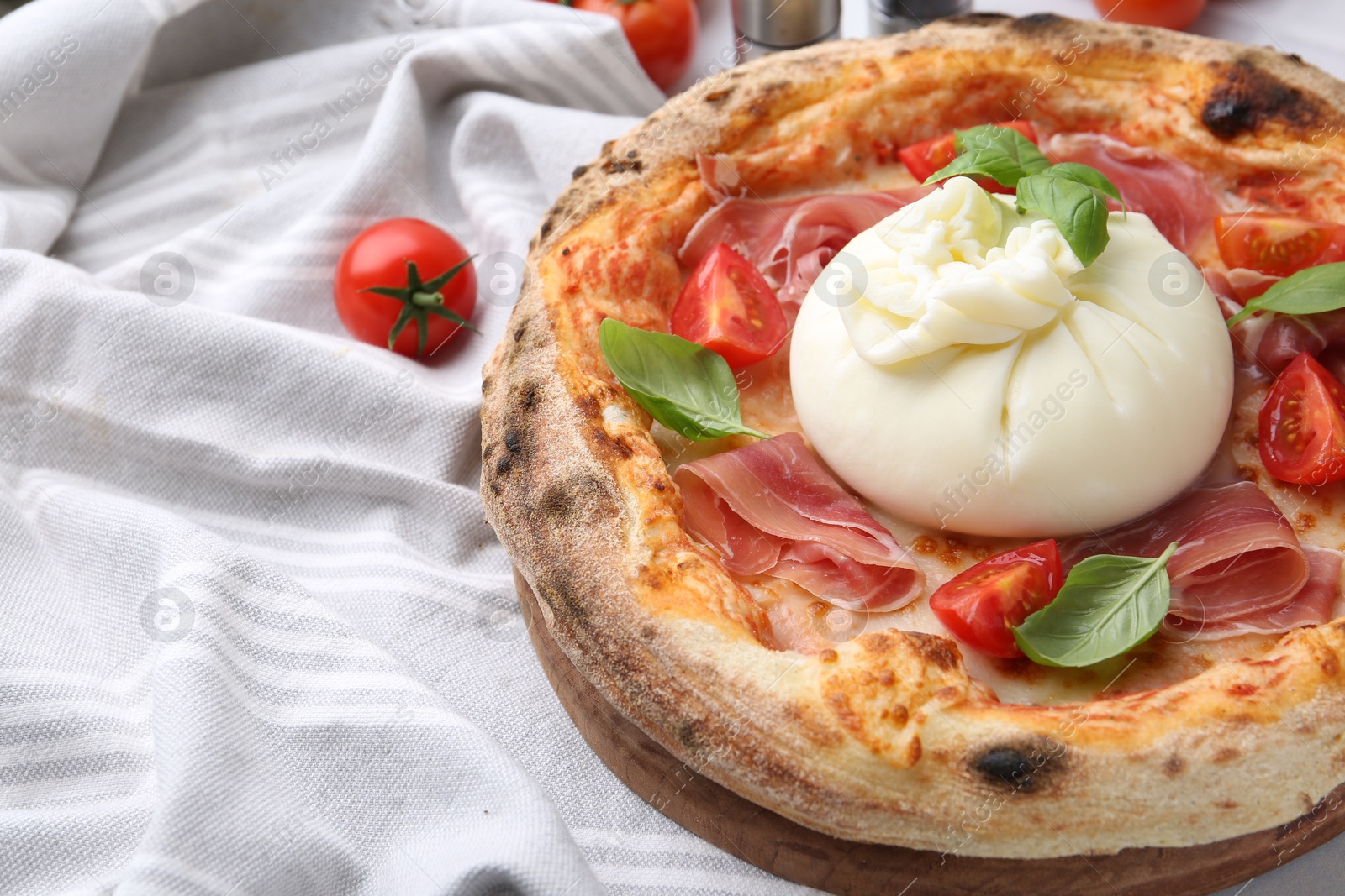 Photo of Delicious pizza with burrata cheese, basil, tomatoes and ham on table, closeup