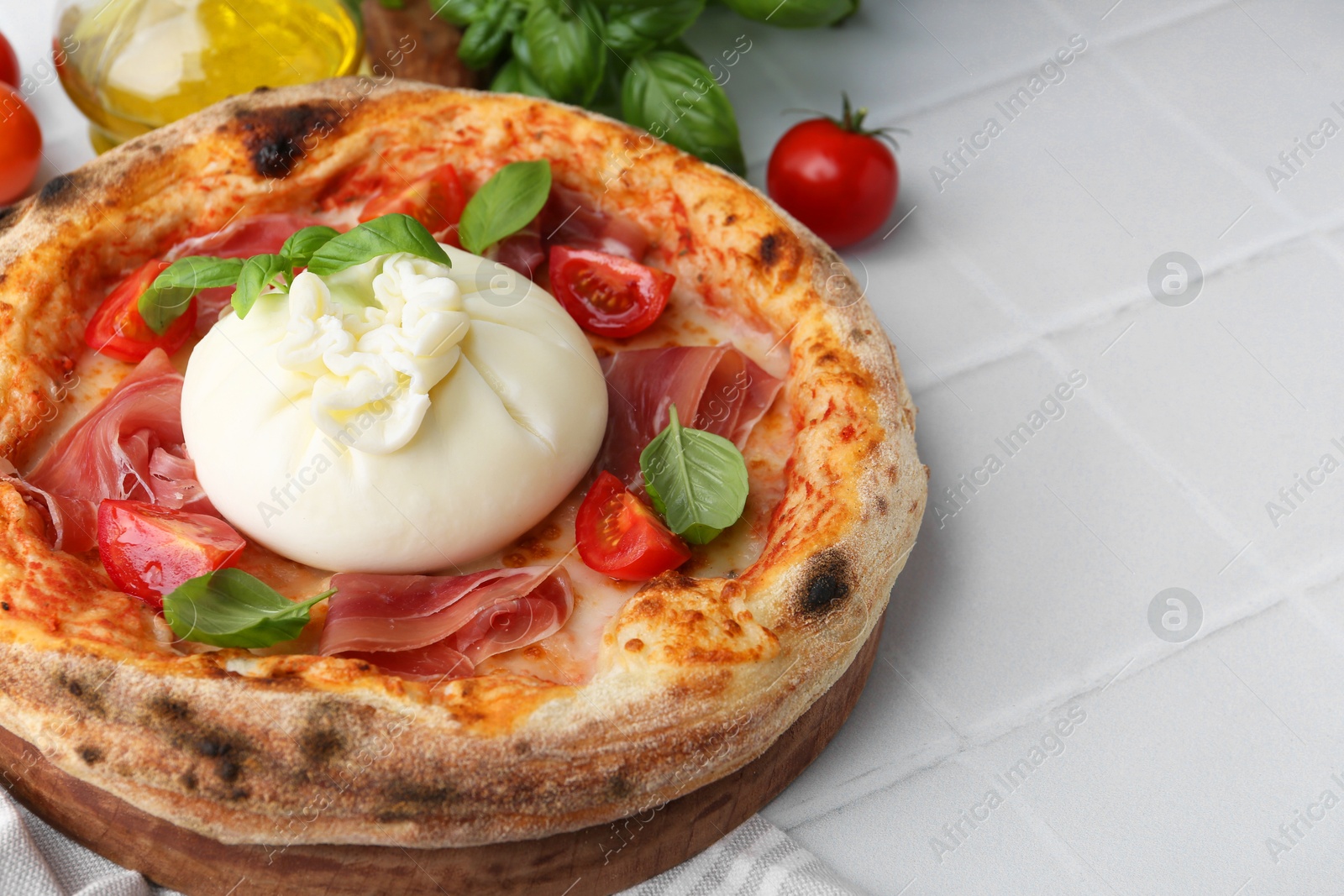 Photo of Delicious pizza with burrata cheese, basil, tomatoes and ham on white tiled table, closeup. Space for text