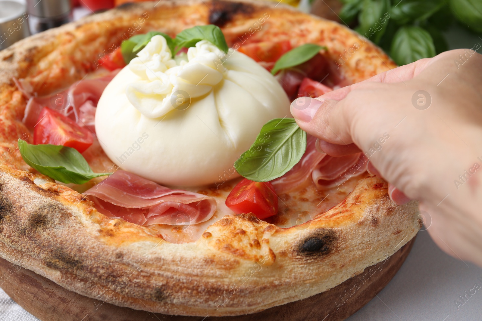 Photo of Woman adding basil to burrata pizza at table, closeup