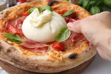 Photo of Woman adding basil to burrata pizza at table, closeup