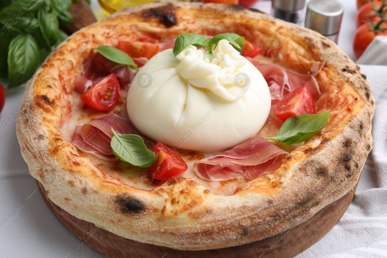 Photo of Delicious pizza with burrata cheese, basil, tomato and ham on table, closeup