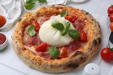 Photo of Delicious pizza with burrata cheese, basil, tomatoes and ham on table, closeup